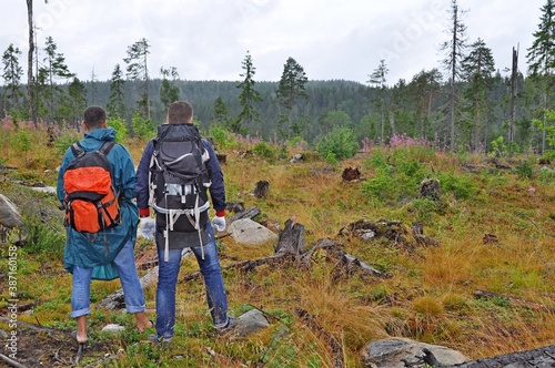 Two men with backpacks travel through the beautiful places of Karelia in cloudy rainy weather.