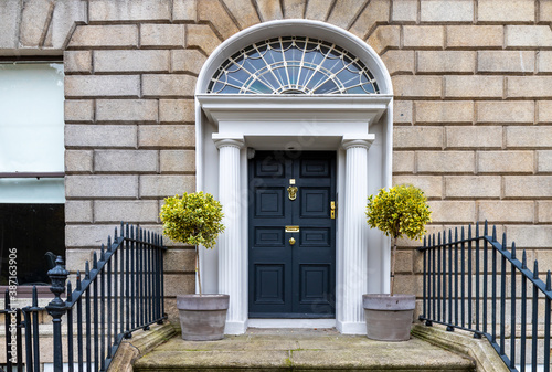 Black paneled Georgian door, with decorative lead fanlight, stone columns and granite steps at building entrance. Two bay trees in planters either side. Dublin, Ireland photo