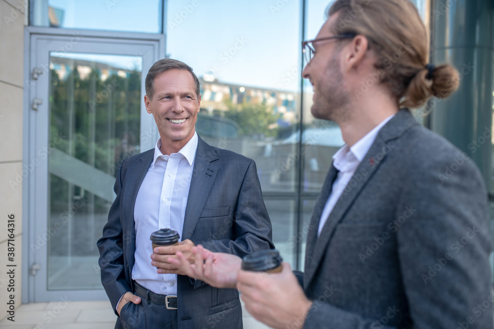 Two male coworkers drinking coffee outside business center, discussing business issues Two male coworkers drinking coffee outside business center, discussing business issues