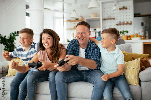 Husband and wife playing video games with joysticks in living room. Loving couple are playing video games with kids at home..
