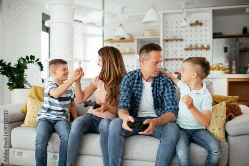 Husband and wife playing video games with joysticks in living room. Loving couple are playing video games with kids at home..