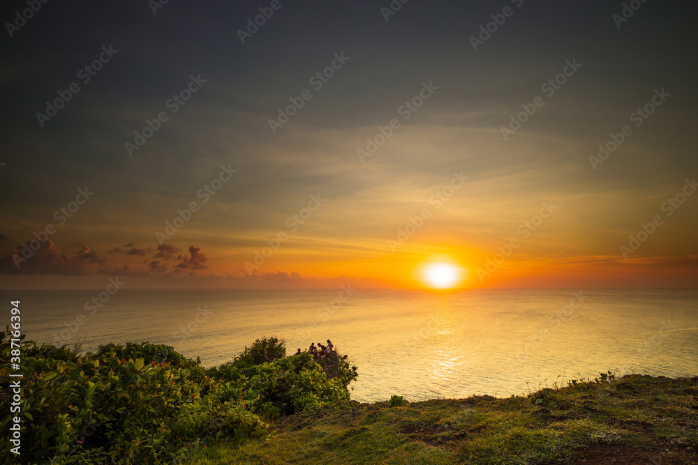 Seascape. Spectacular view from Uluwatu cliff in Bali. Sunset time. Golden hour. Bright sunlight on the horizon. Silhouettes of people. Nature concept. Soft focus. Slow shutter speed.
