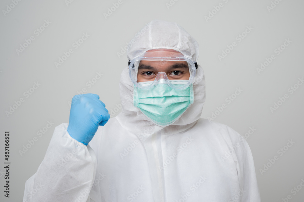 A portrait of virologist Wearing PPE suit erect his fist feel power look into camera isolated on white background. Personal Protective Equipment Concept.