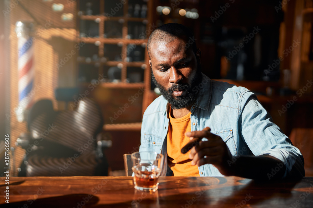 Handsome Afro American man smoking cigar at barbershop bar