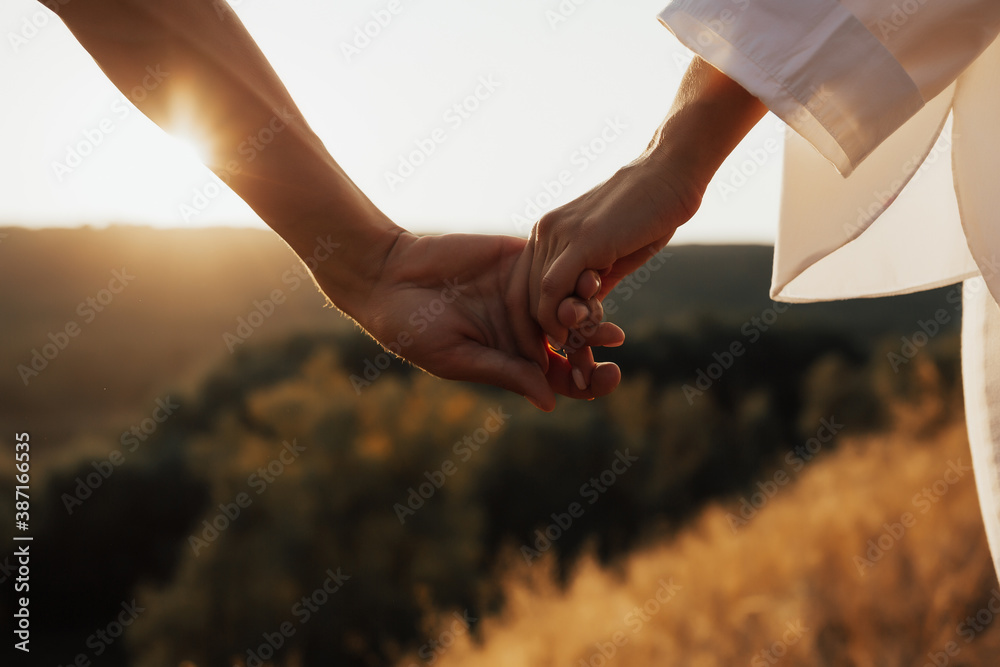 Close-up of hands of the couple. They holding hands at sunset, sunshine.
