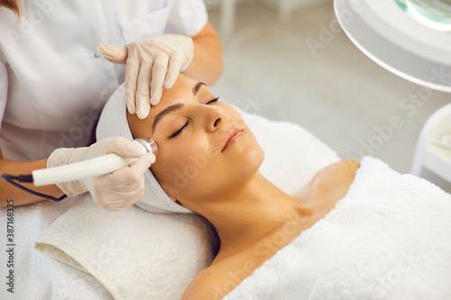 Cosmetologist making vacuum facial skin cleaning for young woman in beauty salon photo