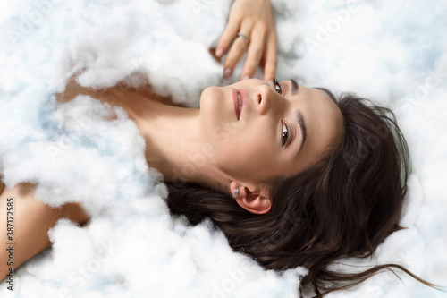 beautiful young brunette woman lies in a cloud covered with a cloud like a blanket