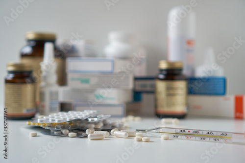 Bottle pills and medicine capsule on table, drugs and tablets boxes in background. Medical thermometer with a temperature of 38 degrees. Increased body temperature of a sick person. 