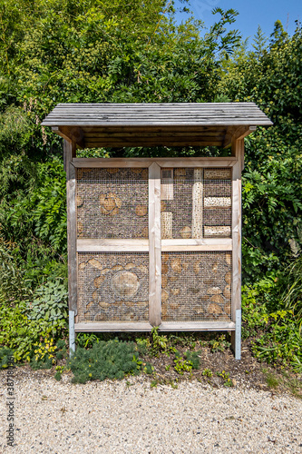 Hotel or insect house made of wood with four square compartments, with metal mesh and pieces of wood of different shape with green vegetation in the background, sunny summer day in a nature reserve