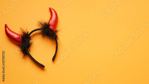 Red devil horns head hoop on orang background. Accessory for Halloween celebration, top view, flat lay, copy space