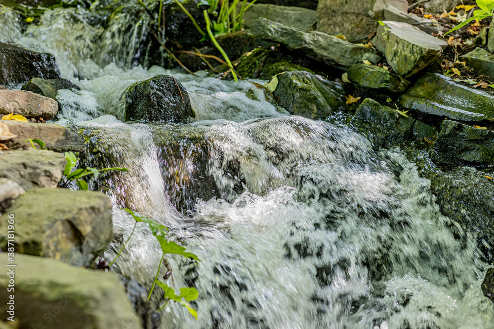 Stream with a small waterfall with the water flowing between the rocks with moss with the sunlight reflecting on the water, sunny day in nature Stream with a small waterfall with the water flowing between the rocks with moss with the sunlight reflecting on the water, sunny day in nature