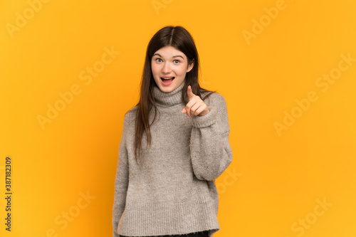 Young Ukrainian girl isolated on yellow background surprised and pointing front © luismolinero