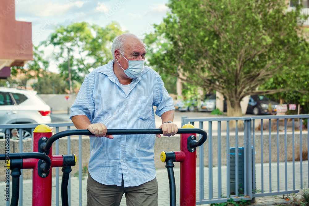 Old man in a face mask likes exercising at an outdoor fitness station near his residence. Elder knows that physical activity boosts immune function. Old man in a face mask likes exercising at an outdoor fitness station near his residence. Elder knows that physical activity boosts immune function.