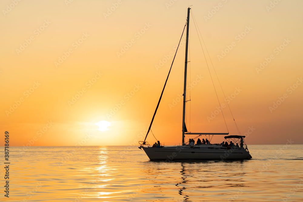 sunset at sea during calm weather with a view of a large yacht with a sail