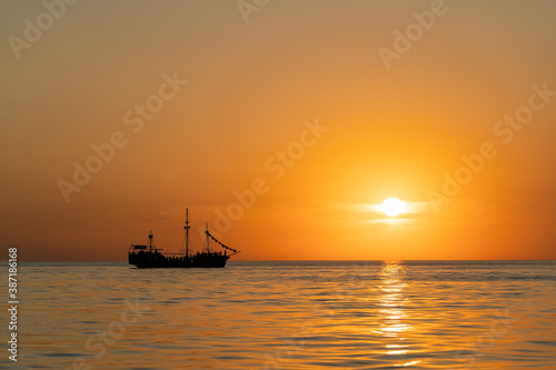 sunset at sea during calm weather with a view of a large yacht with a sail