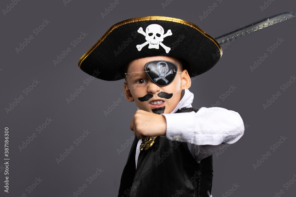 The classic pirate captain character, brandishing a saber. A boy on Halloween dressed in a pirate costume. Halloween holiday concept on gray background