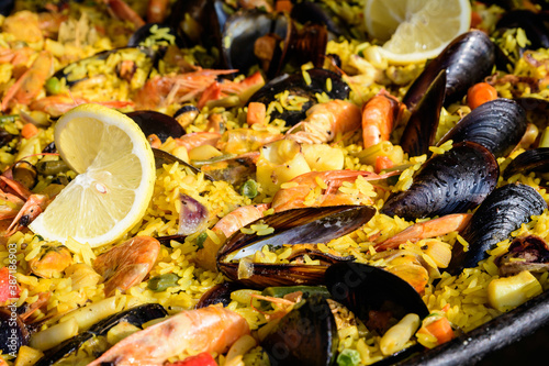 Close up of large portion of traditional Spanish paella dish freshly being cooked with seafood and rice in a frying pan at a street food festival, ready to eat seafood, side view, selective focus.