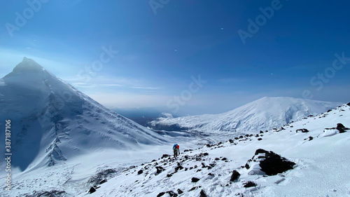 A tourist climbs the Klyuchevskaya Sopka volcano along a snow-covered path past stones.