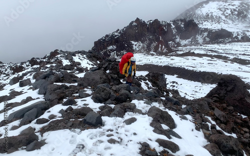 An adventurer-climber with an ice ax goes to the top of the volcano along a snow-covered trail.