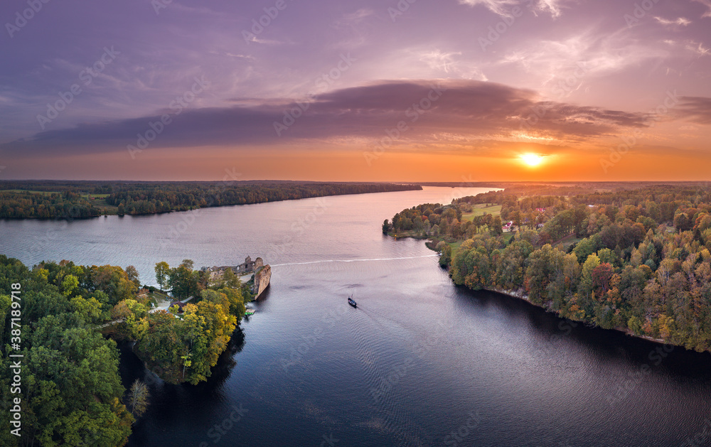 Fototapeta premium Aerial view of Koknese castle ruins at colorful sunset. Medieval ruins on the shore of river surrounded by forest.