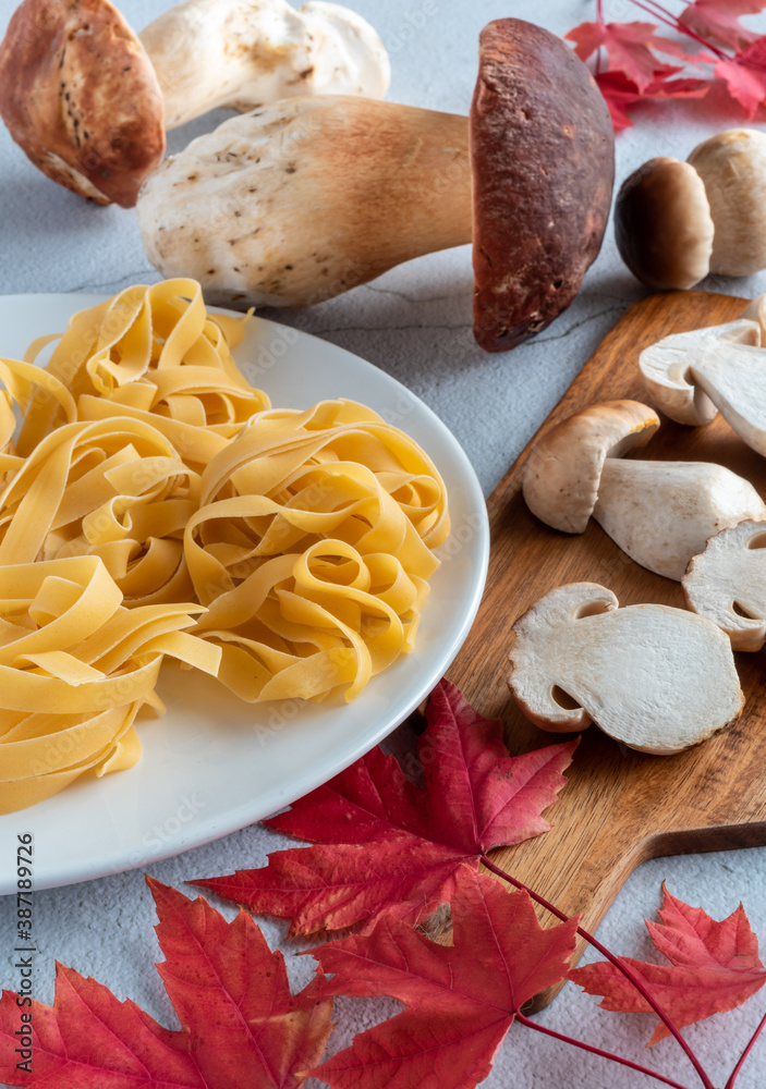 Fototapeta premium View of boletus edulis with pasta tagliatelle. There are red leaves and a cutting board