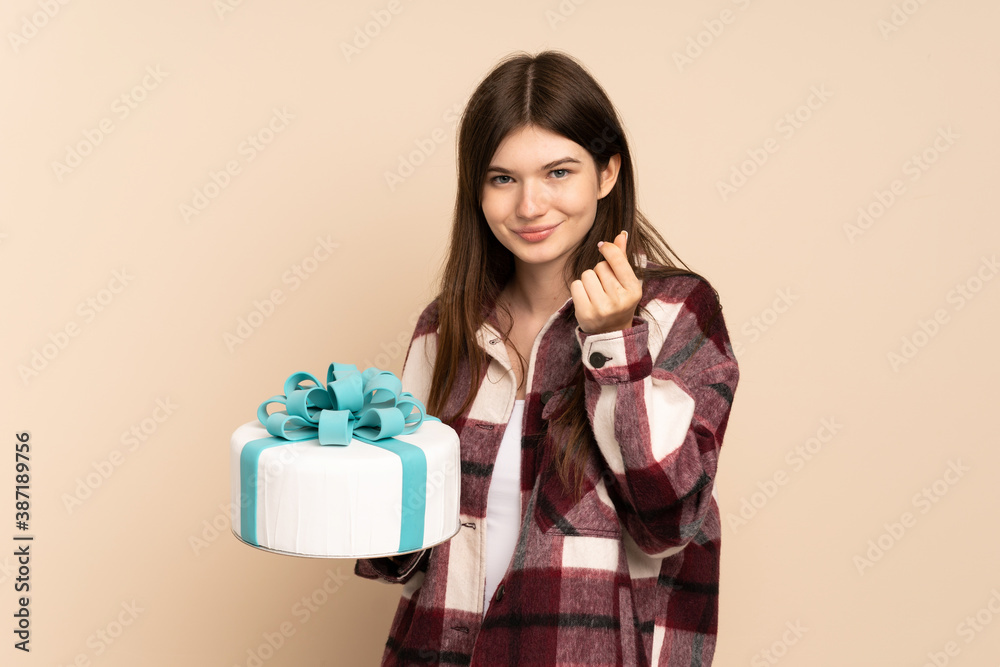 Young Ukrainian girl holding a big cake isolated on beige background making money gesture Young Ukrainian girl holding a big cake isolated on beige background making money gesture