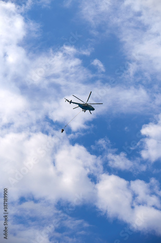 Fire fighting helicopter with water bucket on a cloudy sky background