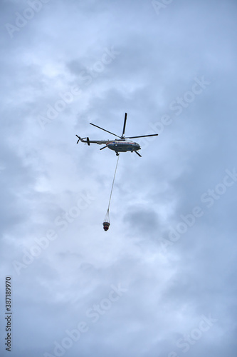 Fire fighting helicopter with water bucket on a gloomy sky background