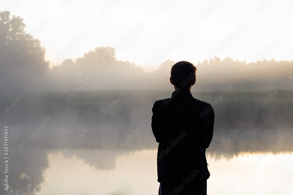 Man meets the dawn near the pond in the fog, early morning. Photo from behind Man meets the dawn near the pond in the fog, early morning. Photo from behind