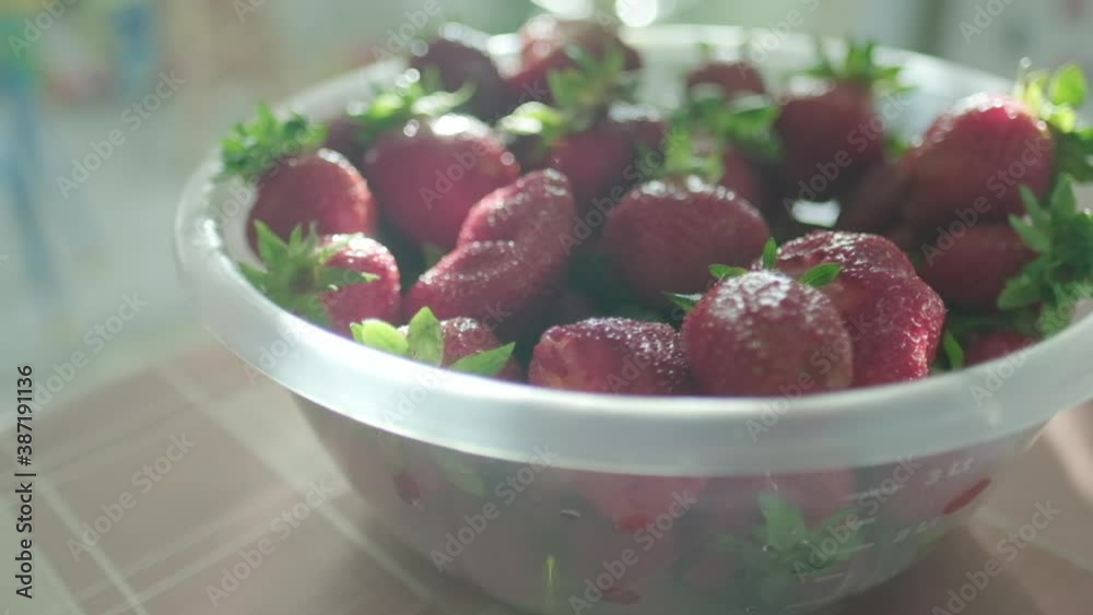A plastic bowl with red strawberry on the table near window at sunny day A plastic bowl with red strawberry on the table near window at sunny day