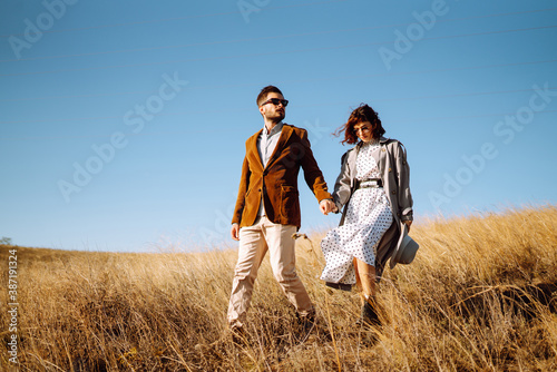 Stylish  young couple enjoying autumn weather in autumn field. Lovely couple walking and hugging in the field together. The concept of youth  love and lifestyle.
