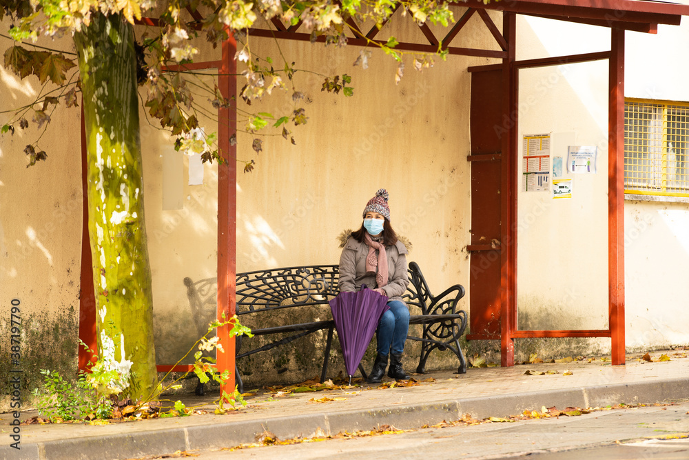 Woman with umbrella sitting at the bus stop