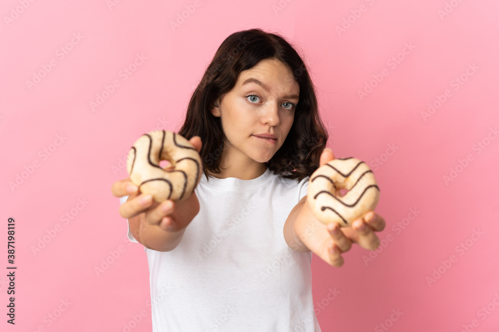 Teenager Ukrainian girl isolated on pink background holding a donut and sad