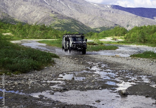 SUV rides on a mountain stream among the mountains in the summer