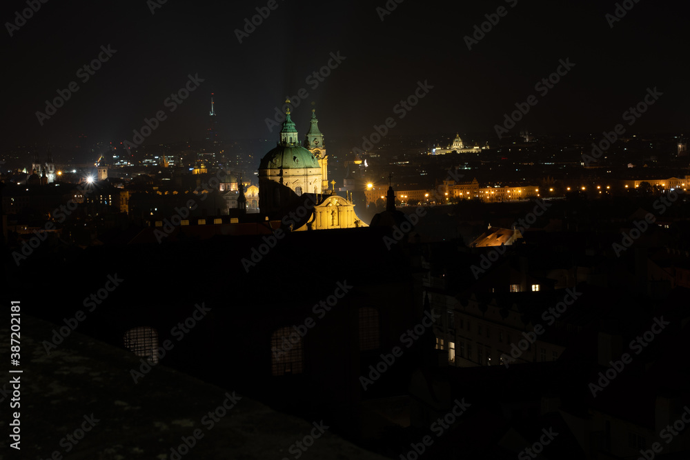
The tower of the Church of St. Nicholas is a Baroque church located in Prague from 1625 in the center of Prague. in the background a view of street lights in the city at night