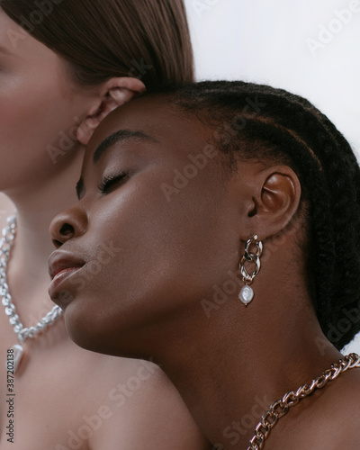 Сlose-up portrait of africans and europeans girls in jewelry on neck and with ear in ears. Two beautiful girls of different races dark skinned and white skinned with nutural make up photo