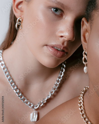 Сlose-up portrait of africans and europeans girls in jewelry on neck and fashionable make up. Two beautiful girls of different races dark skinned and white skinned with nutural make up