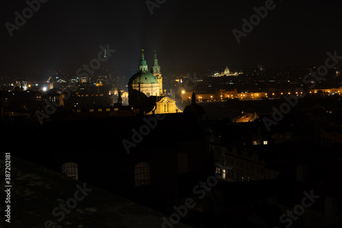  The tower of the Church of St. Nicholas is a Baroque church located in Prague from 1625 in the center of Prague. in the background a view of street lights in the city at night