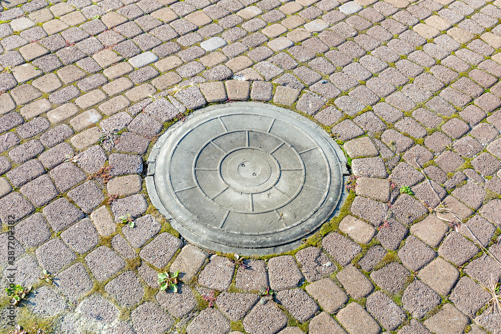 Old iron sewer manhole among the cobblestones of the pavement Old iron sewer manhole among the cobblestones of the pavement