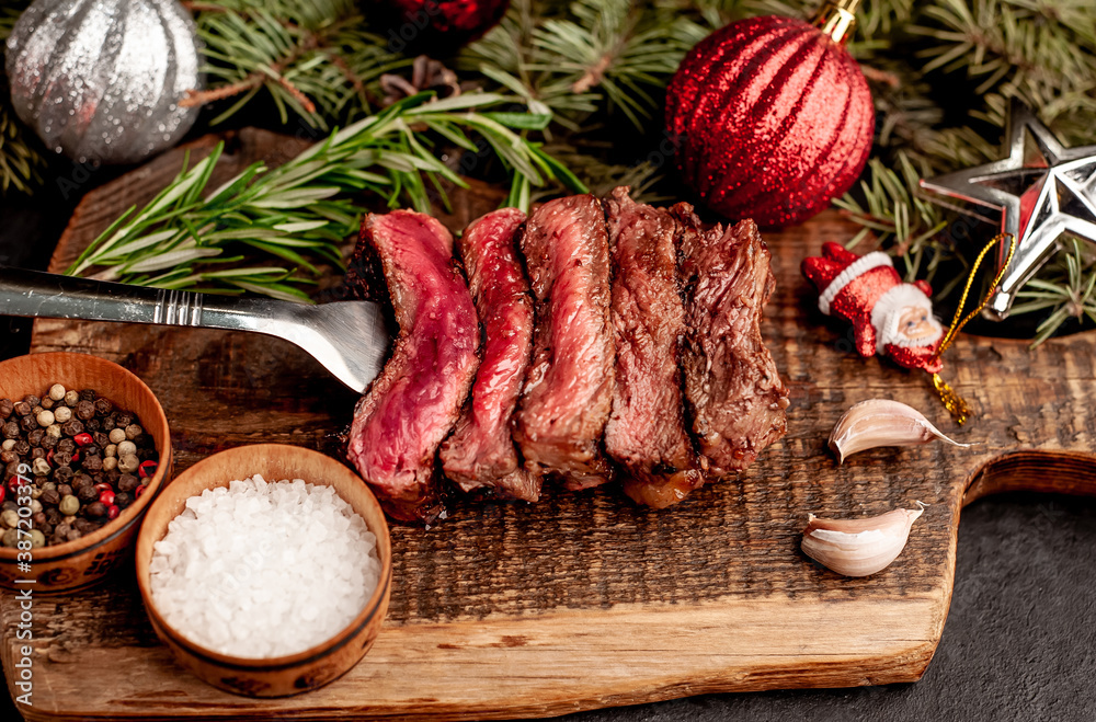 Different degrees of roasting of steak on a meat fork for Christmas on a background of a stone with a spruce and Christmas toys 