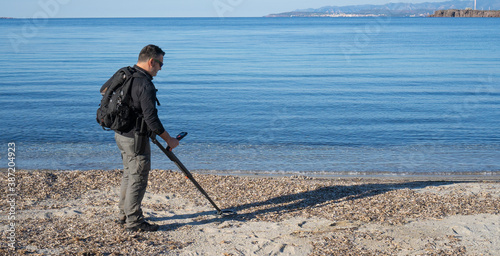  man uses the metal decector at the beach to search for precious objects