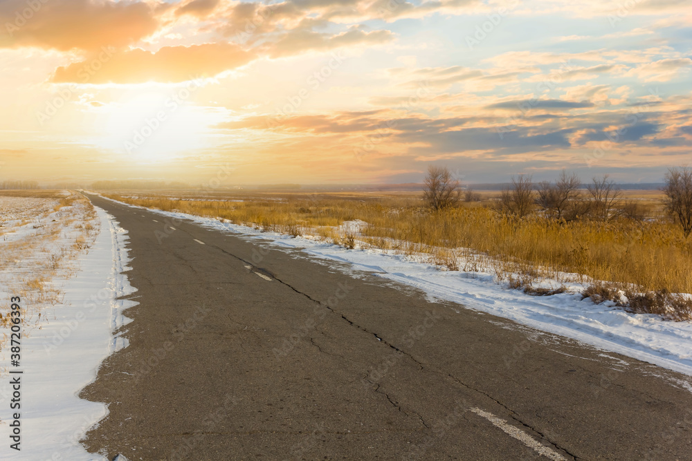 asphalt road among a snowbound prairie at the sunset asphalt road among a snowbound prairie at the sunset