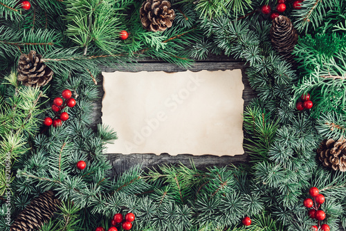 Blank old paper, fir tree branches, red berries and pinecone on wooden background. Christmas background
