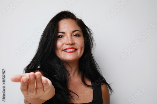 Headshot of happy mature woman holding out her hand  wearing black T-shirt  smiling. Isolated on white background wall.