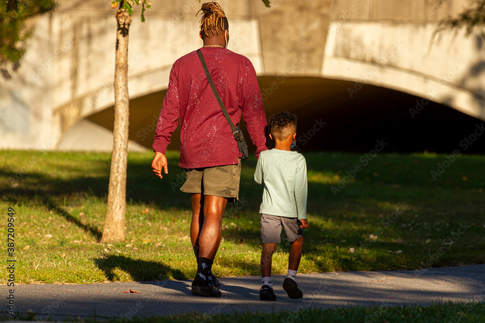 A young African American father holds hands of his son as they walk ...