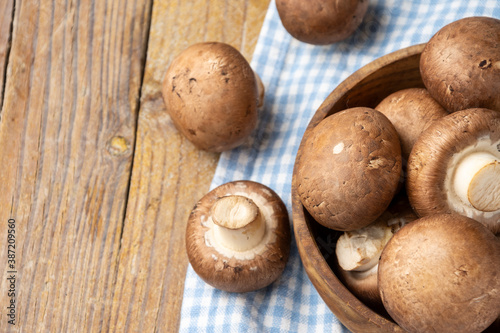 Aerial view of portobello mushrooms in wooden bowl, with selective focus, on blue checkered cloth, on rustic wooden table, horizontal, with copy space
