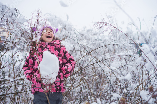 A little girl laughs loudly at a big snowball. A child rejoices in snow