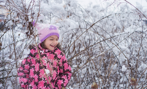 The child rejoices in the snow in a wild field among thickets. Stylish and beautiful European girl