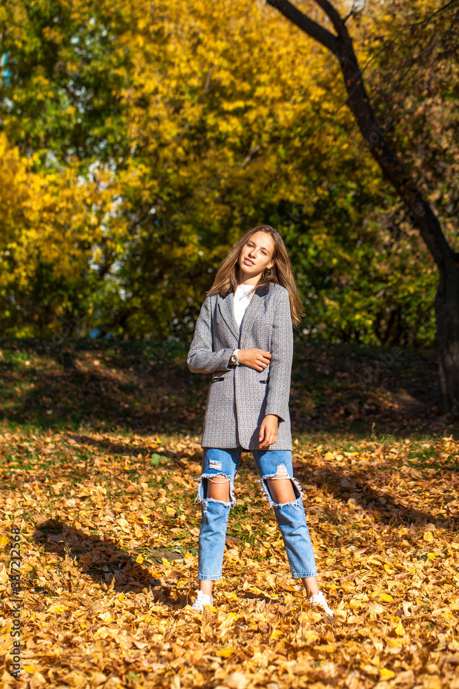 Portrait of a young blonde girl in stylish ripped jeans posing in an autumn park Portrait of a young blonde girl in stylish ripped jeans posing in an autumn park