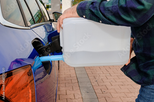 Man filling a diesel engine fluid from canister into the tank of blue car. Diesel exhaust fluid for reduction of air pollution. 